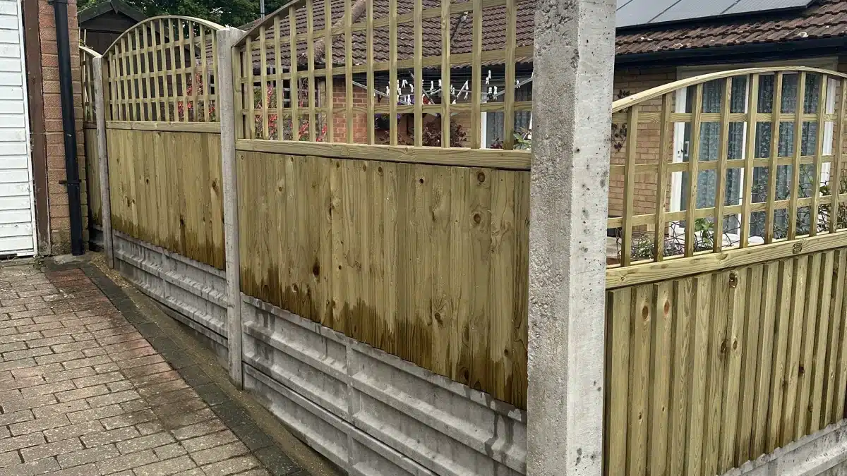 Wooden garden fence with concrete posts beside a paved driveway