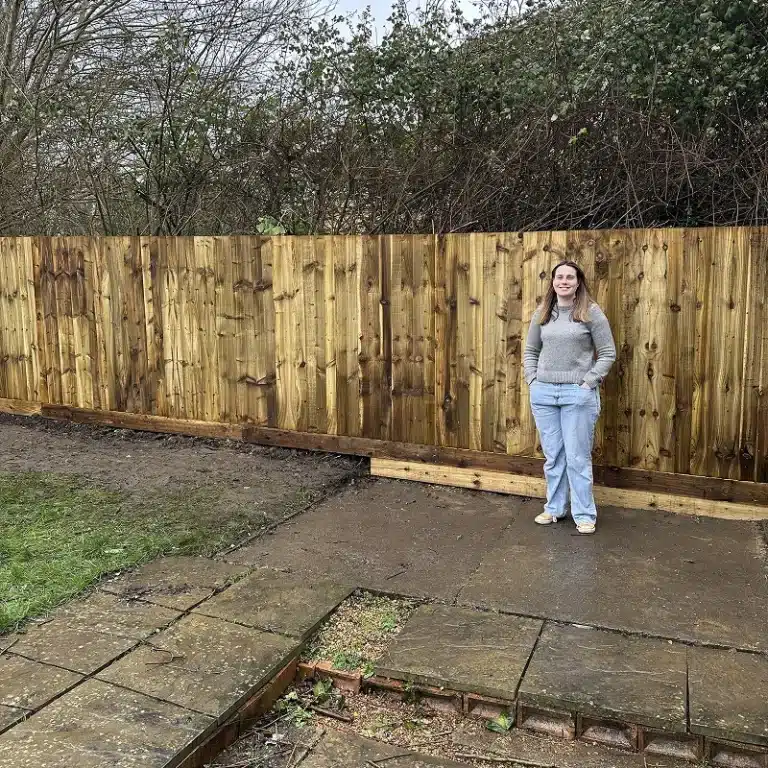 Woman standing in a garden beside a newly installed wooden fence