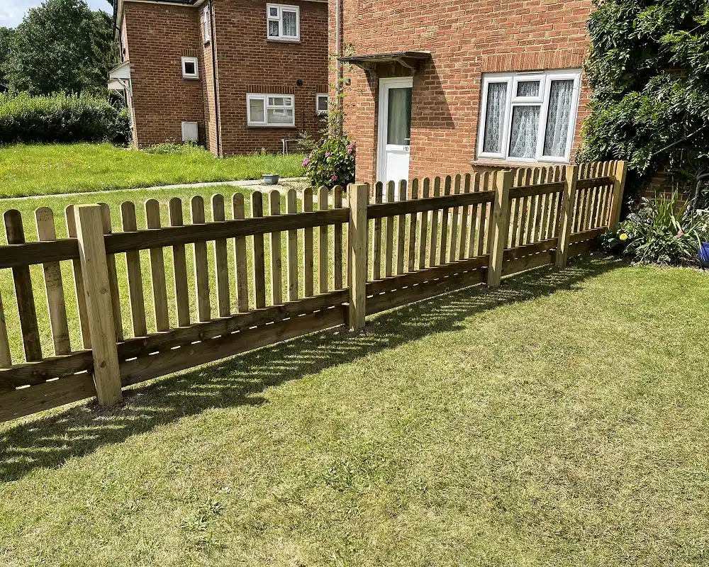 Wooden picket fence in a front garden beside a brick house