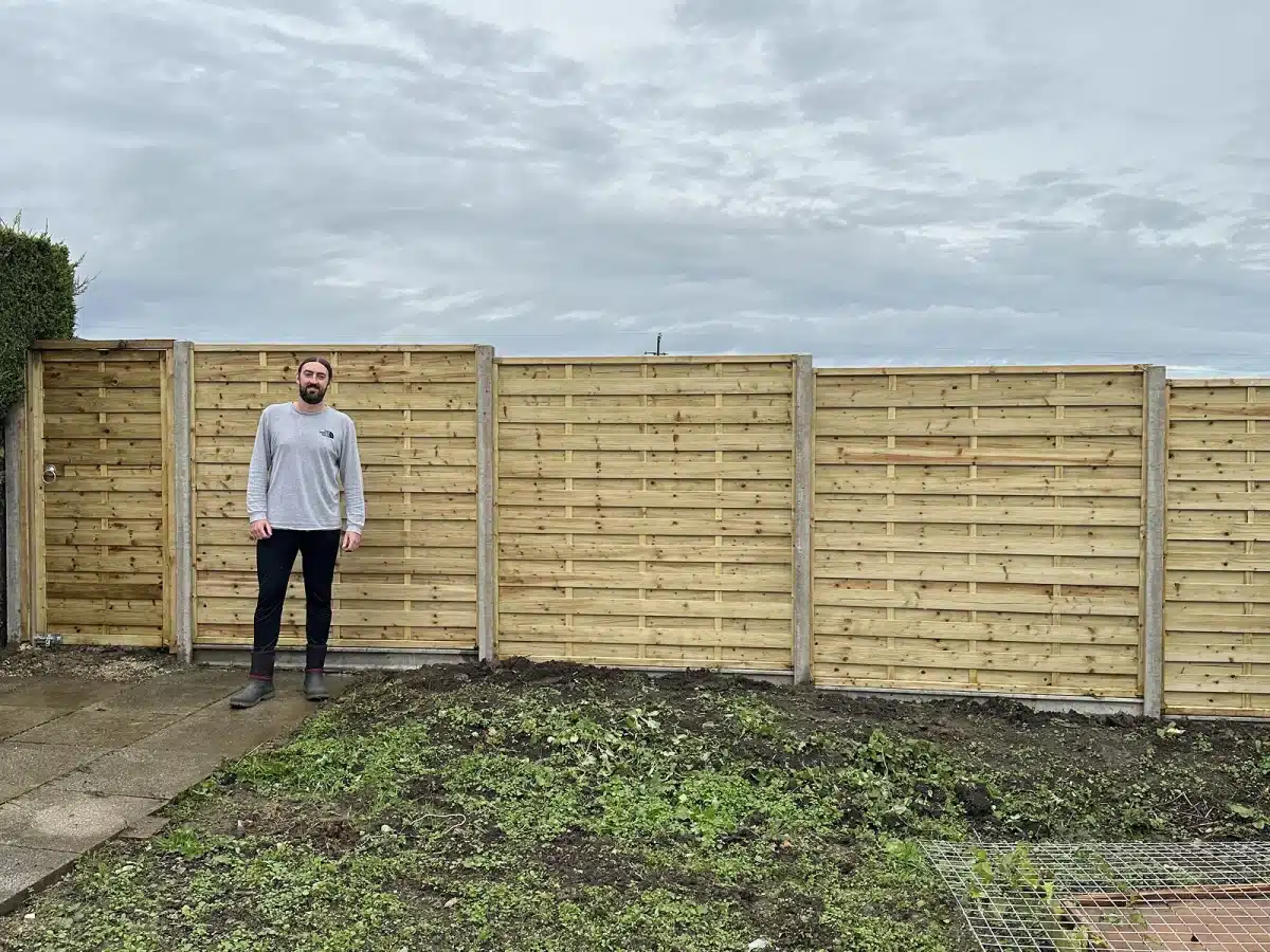 Man standing in a garden in front of a newly installed wooden fence