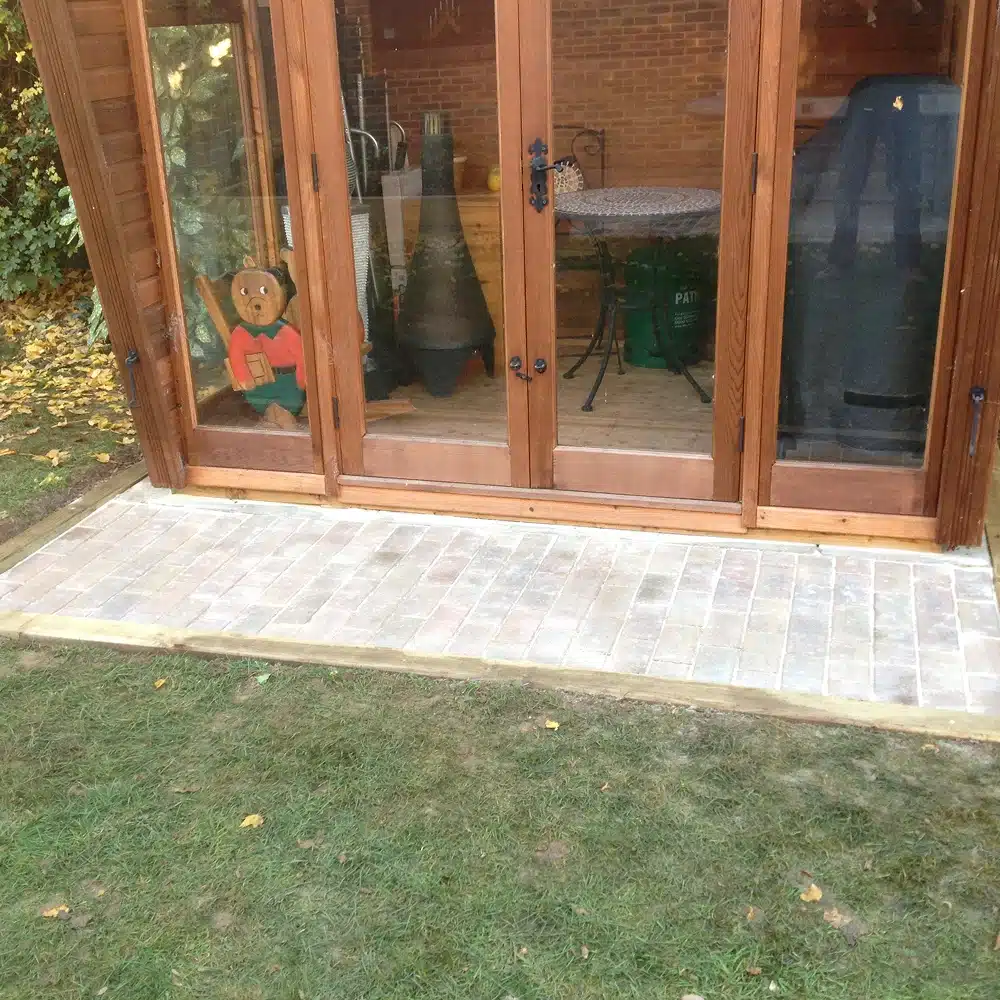 Wooden patio doors opening onto a paved patio and lawn, with a teddy bear visible inside