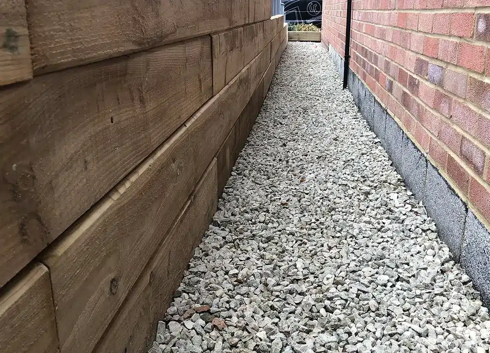 Narrow gravel path between a timber retaining wall and a brick house wall