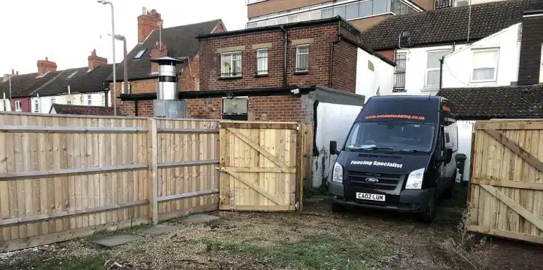 Van parked in a yard beside newly installed wooden fencing and gates
