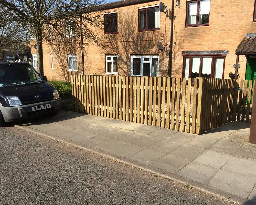 A black van parked beside a wooden fence in front of a brick house