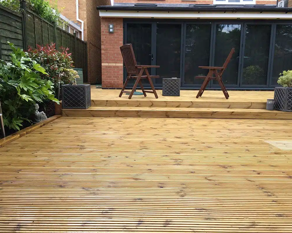 Wooden garden deck with two chairs and potted plants outside a house