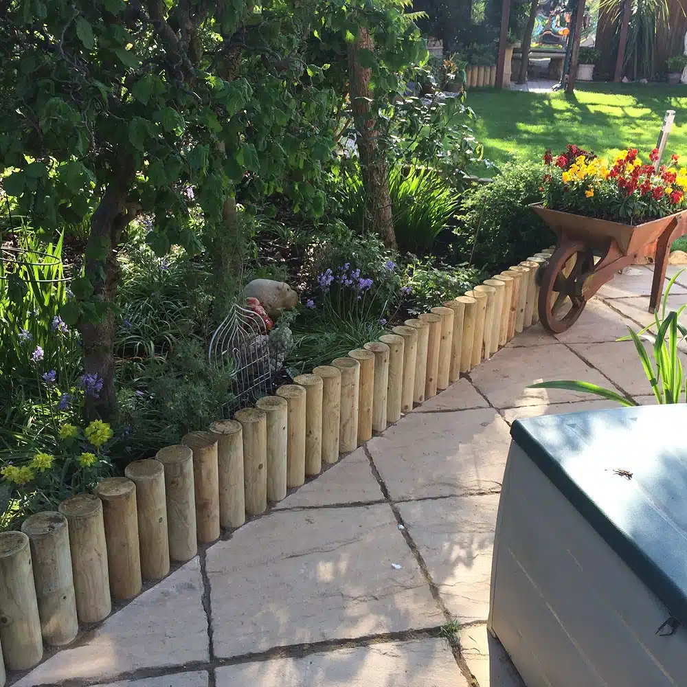 Garden path beside a flower bed, with a wheelbarrow planter and a wooden log border