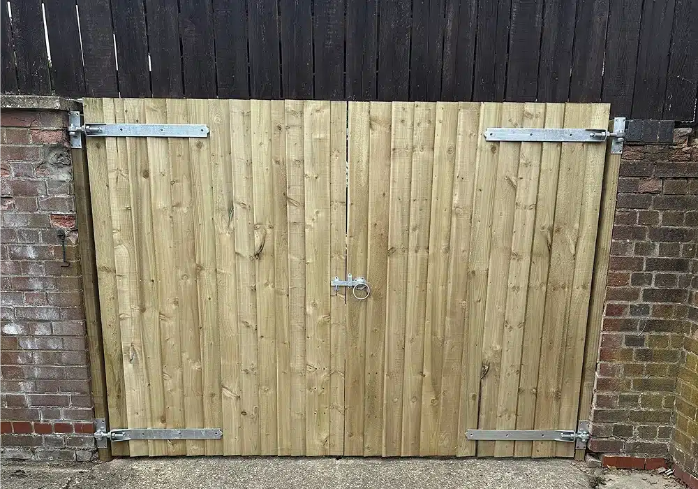 Wooden double gate with metal hinges and a central latch between brick walls