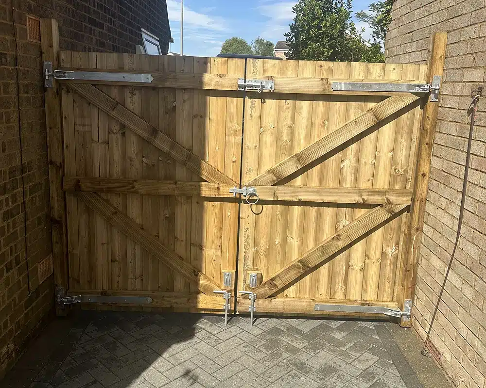 Wooden double driveway gate with metal hinges and a central latch between brick walls