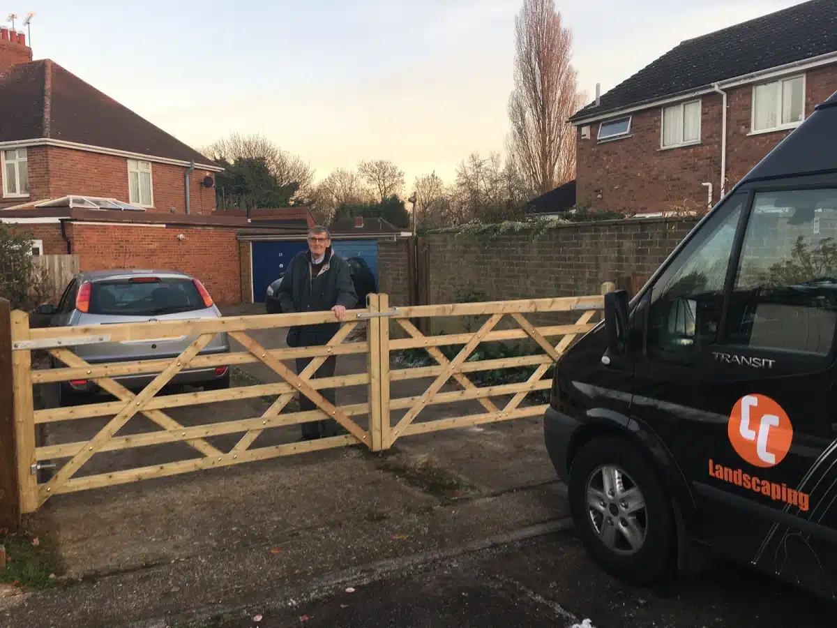 Man standing by a newly fitted wooden driveway gate beside a landscaping van