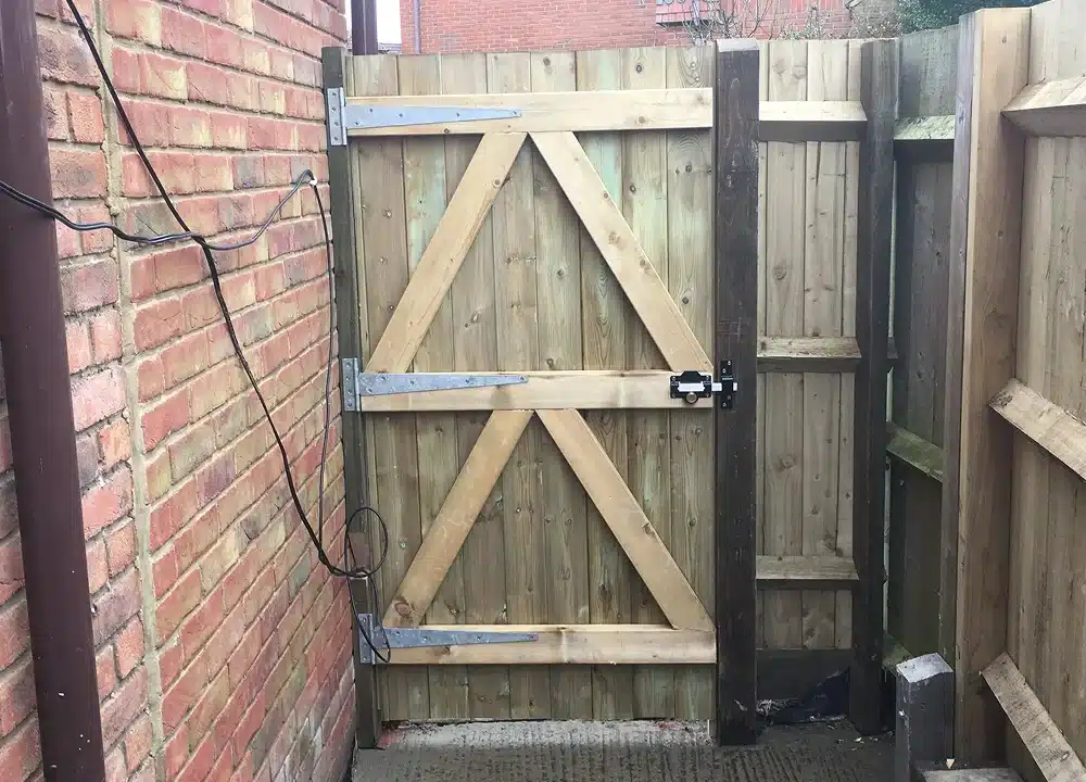 Wooden garden gate between brick walls and fencing